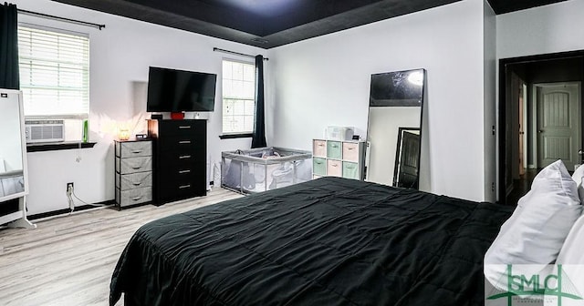 bedroom with cooling unit, light hardwood / wood-style floors, and a tray ceiling