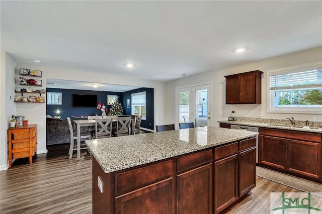 kitchen with light wood-type flooring, a center island, light stone countertops, and sink