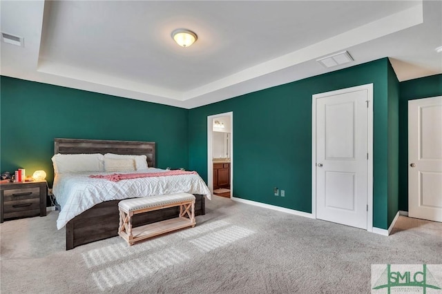 bedroom featuring a raised ceiling, light carpet, and connected bathroom