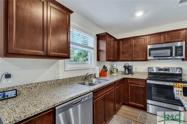 kitchen featuring light stone countertops, stainless steel appliances, light hardwood / wood-style flooring, and sink