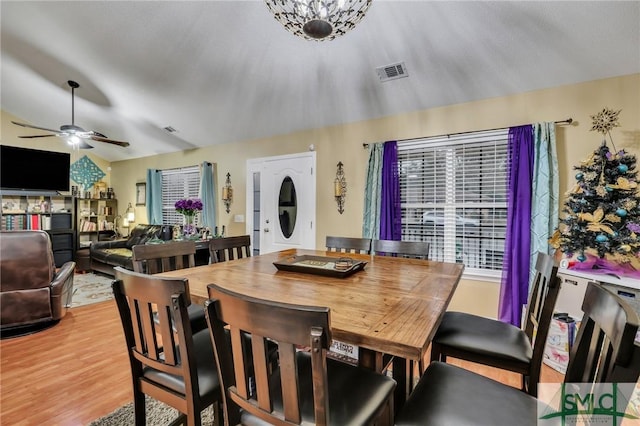 dining space with ceiling fan with notable chandelier, light hardwood / wood-style floors, and vaulted ceiling