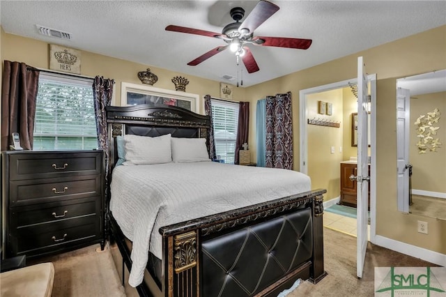 bedroom featuring ceiling fan, light colored carpet, a textured ceiling, and ensuite bath