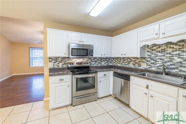 kitchen with a textured ceiling, stainless steel appliances, sink, white cabinetry, and light tile patterned flooring