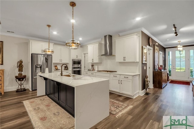 kitchen with pendant lighting, white cabinets, a center island with sink, wall chimney range hood, and stainless steel appliances