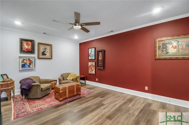 living area with wood-type flooring, ceiling fan, and ornamental molding