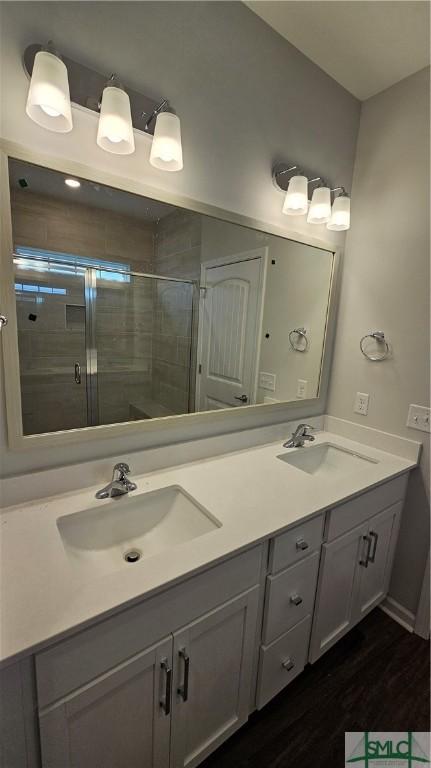 bathroom with double vanity, a shower stall, a sink, and wood finished floors