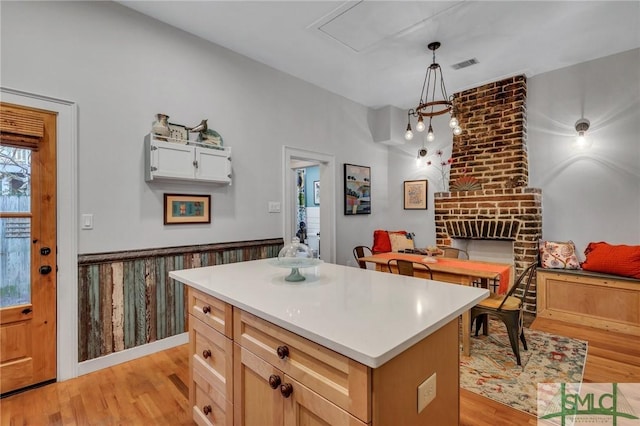 kitchen featuring light wood-type flooring, pendant lighting, a fireplace, a center island, and white cabinetry