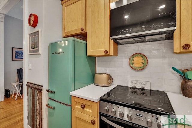 kitchen featuring decorative backsplash, range with electric cooktop, range hood, and fridge