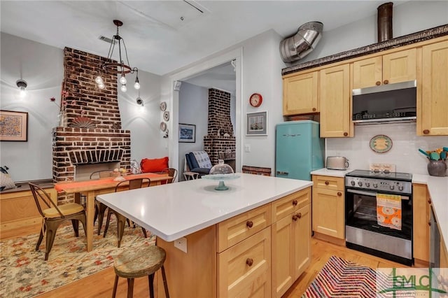 kitchen with a kitchen bar, a brick fireplace, decorative light fixtures, a kitchen island, and stainless steel range with electric cooktop