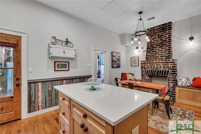 kitchen with a brick fireplace, decorative light fixtures, white cabinetry, light hardwood / wood-style floors, and a kitchen island