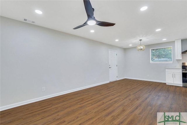 unfurnished living room featuring ceiling fan with notable chandelier and dark wood-type flooring