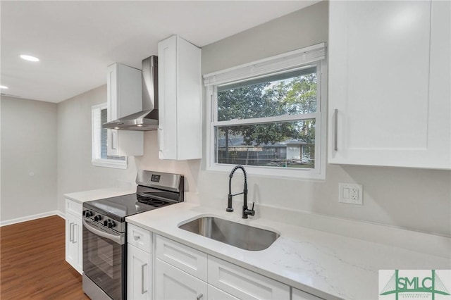 kitchen featuring wall chimney range hood, sink, light stone countertops, stainless steel range oven, and white cabinetry