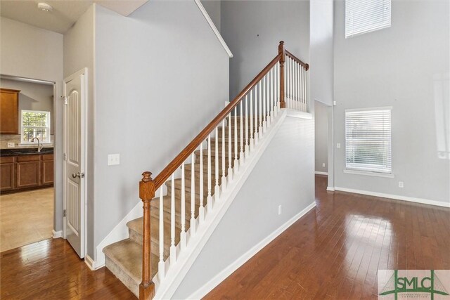 stairs featuring wood-type flooring, sink, and a high ceiling