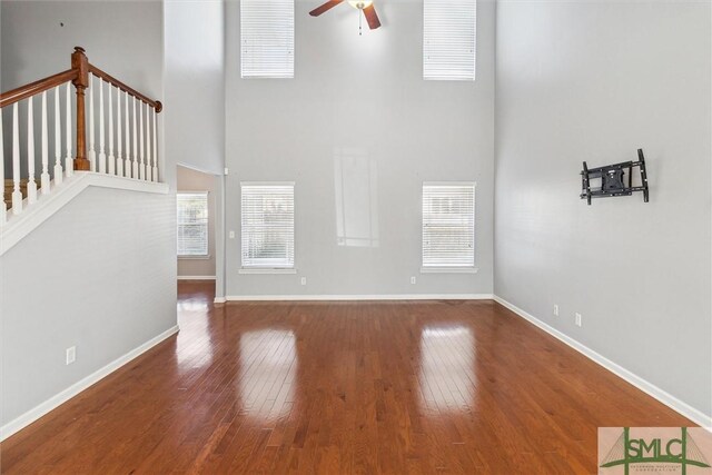 unfurnished living room featuring hardwood / wood-style flooring, ceiling fan, and a towering ceiling