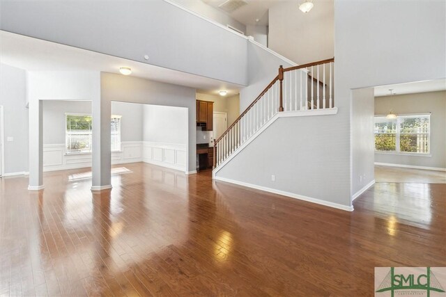 unfurnished living room with ornate columns, plenty of natural light, and dark wood-type flooring