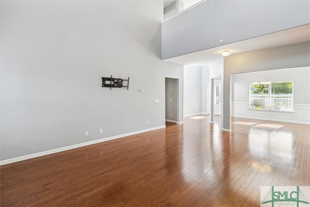 unfurnished living room with wood-type flooring, a towering ceiling, and a notable chandelier