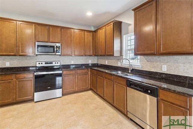 kitchen with backsplash, stainless steel appliances, dark stone countertops, and sink