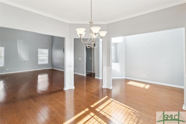 empty room with crown molding, wood-type flooring, and an inviting chandelier