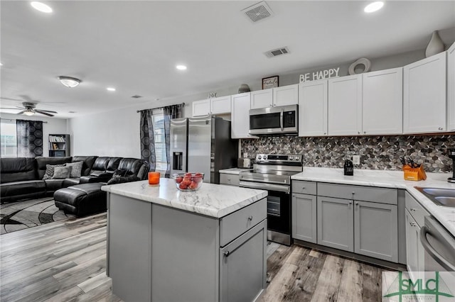 kitchen with appliances with stainless steel finishes, ceiling fan, light hardwood / wood-style floors, a kitchen island, and plenty of natural light