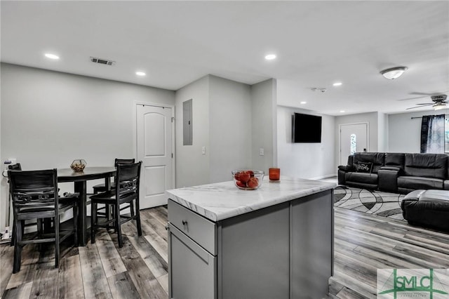 kitchen with light hardwood / wood-style floors, ceiling fan, gray cabinets, electric panel, and a kitchen island