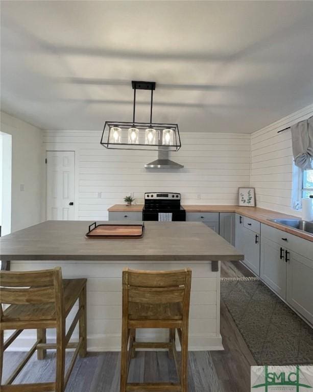 kitchen with butcher block countertops, hanging light fixtures, stainless steel range with electric stovetop, and a breakfast bar area