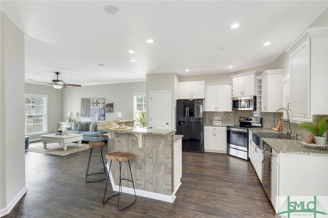 kitchen featuring white cabinets, stainless steel appliances, a kitchen island, and light stone countertops