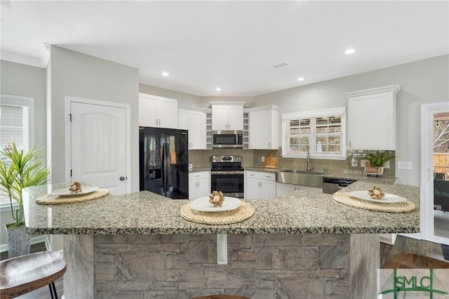 kitchen featuring light stone countertops, sink, stainless steel appliances, a breakfast bar, and white cabinets