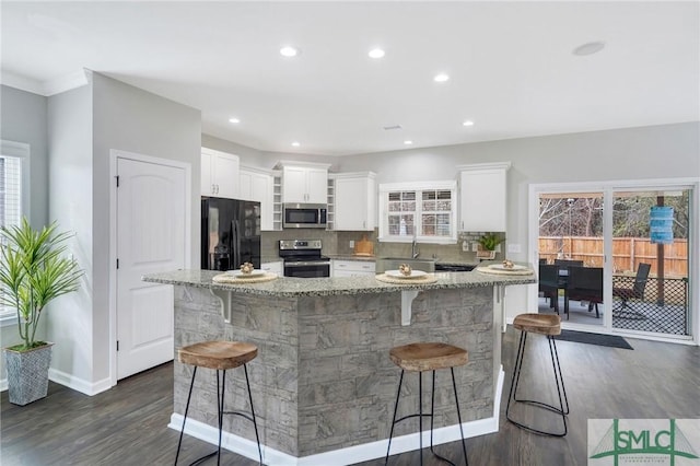 kitchen featuring light stone countertops, appliances with stainless steel finishes, a healthy amount of sunlight, a kitchen bar, and white cabinetry