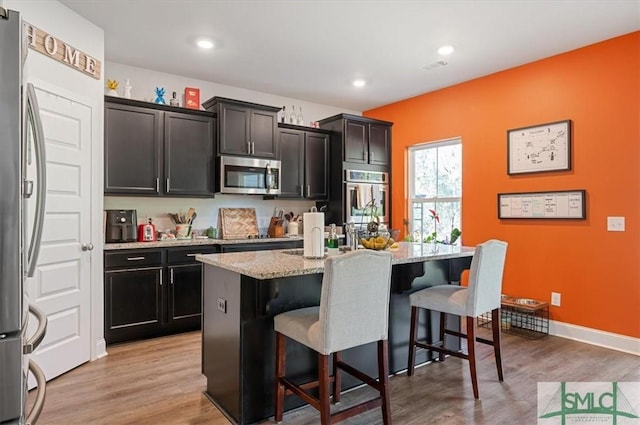 kitchen featuring light hardwood / wood-style floors, a kitchen bar, an island with sink, and appliances with stainless steel finishes