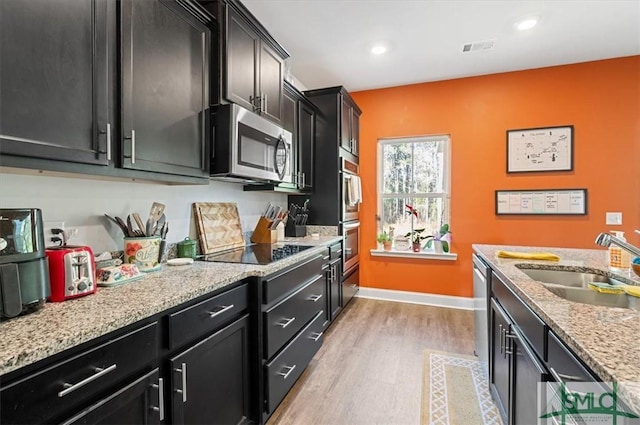 kitchen featuring light stone counters, sink, stainless steel appliances, and light hardwood / wood-style flooring