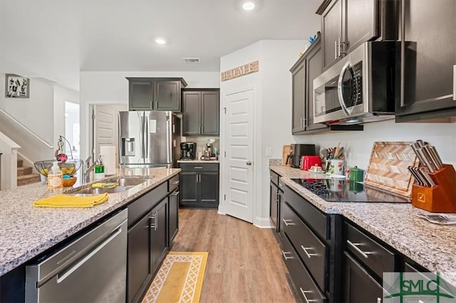 kitchen with light hardwood / wood-style floors, light stone counters, sink, and appliances with stainless steel finishes