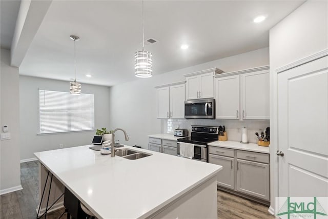 kitchen with stainless steel appliances, sink, wood-type flooring, pendant lighting, and an island with sink