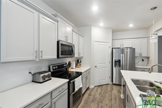 kitchen with backsplash, stainless steel appliances, sink, wood-type flooring, and hanging light fixtures