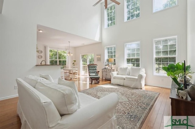 living room with a high ceiling, ceiling fan with notable chandelier, and light hardwood / wood-style flooring