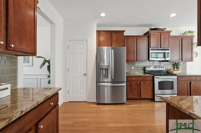 kitchen with light stone countertops, appliances with stainless steel finishes, light wood-type flooring, and tasteful backsplash