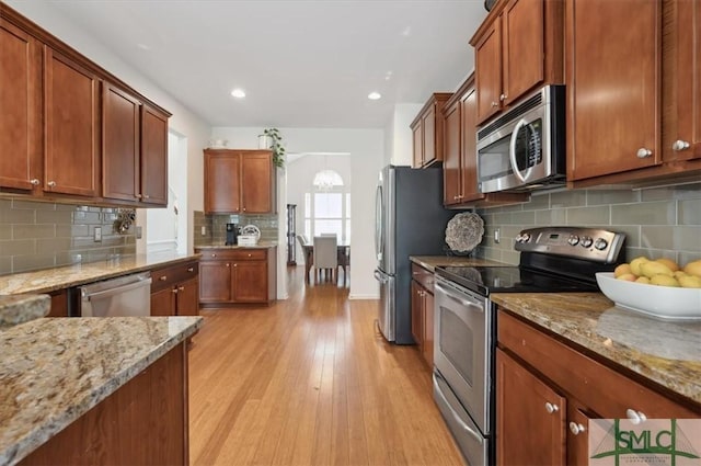 kitchen with tasteful backsplash, light stone counters, stainless steel appliances, and light hardwood / wood-style floors