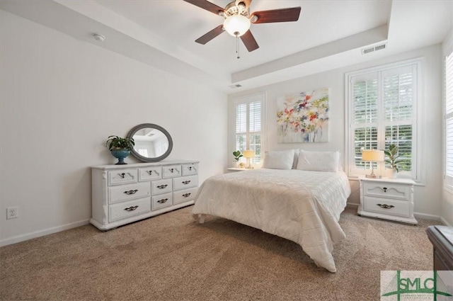 carpeted bedroom with a tray ceiling and ceiling fan