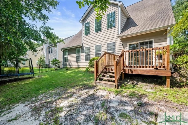 back of property featuring a trampoline, a yard, and a wooden deck