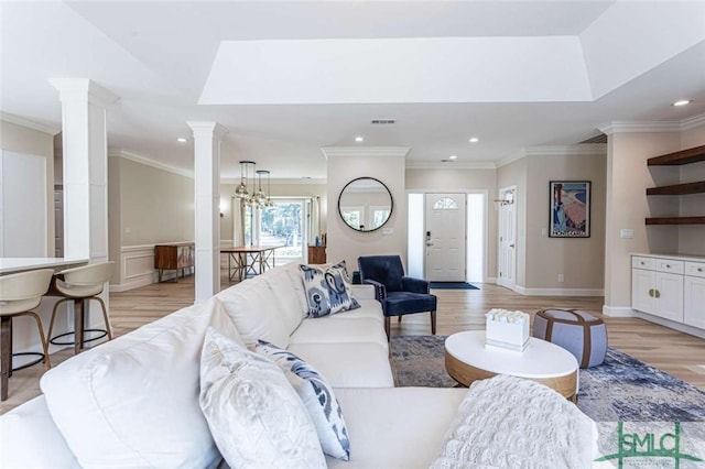 living room featuring light wood-type flooring, a tray ceiling, crown molding, and a notable chandelier