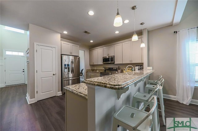 kitchen featuring hanging light fixtures, light stone counters, kitchen peninsula, a kitchen bar, and appliances with stainless steel finishes