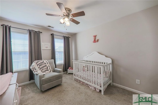 carpeted bedroom featuring multiple windows, a nursery area, and ceiling fan