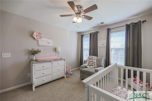 bedroom featuring ceiling fan, a crib, and light carpet