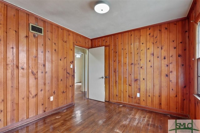 spare room with wood walls, crown molding, and dark wood-type flooring