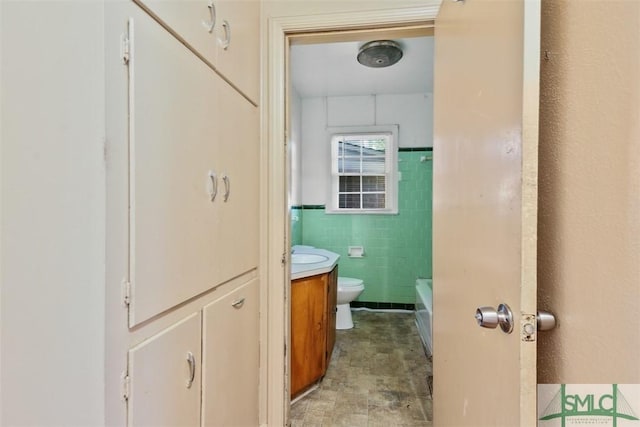 bathroom featuring vanity, a bath, toilet, and tile walls