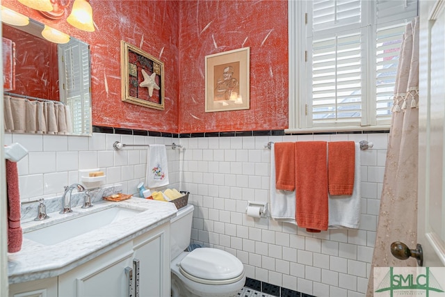 bathroom featuring vanity, toilet, and tile walls