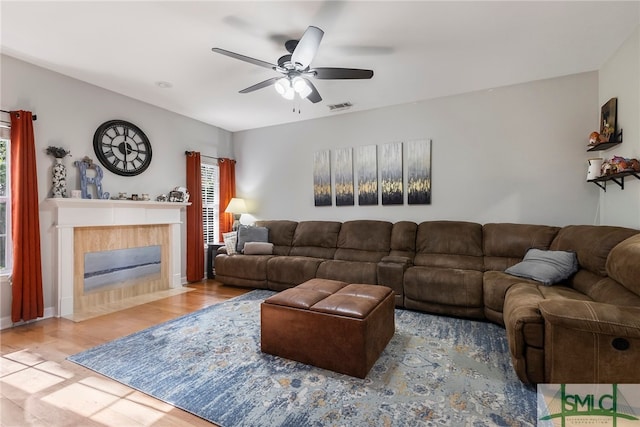 living room featuring ceiling fan, wood-type flooring, and a tile fireplace