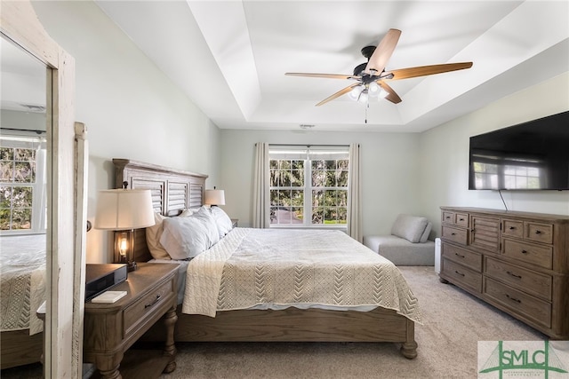 bedroom featuring light colored carpet, a raised ceiling, and ceiling fan