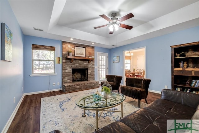 living room with ceiling fan, dark hardwood / wood-style floors, a raised ceiling, and a fireplace