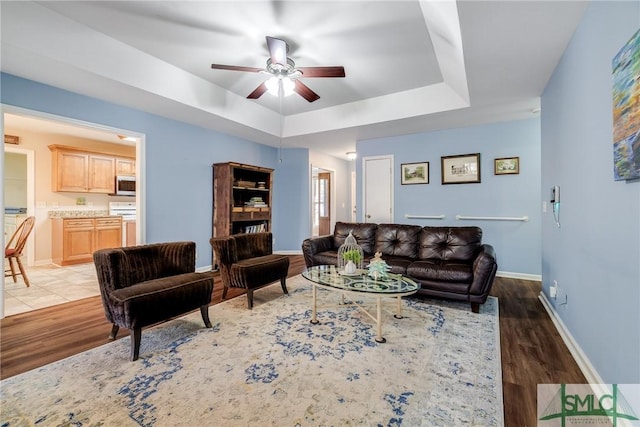 living room featuring ceiling fan, dark hardwood / wood-style floors, and a tray ceiling