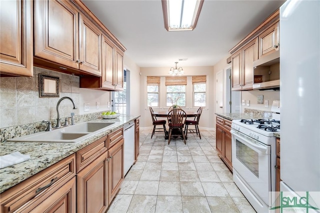 kitchen with sink, an inviting chandelier, light stone counters, pendant lighting, and white appliances